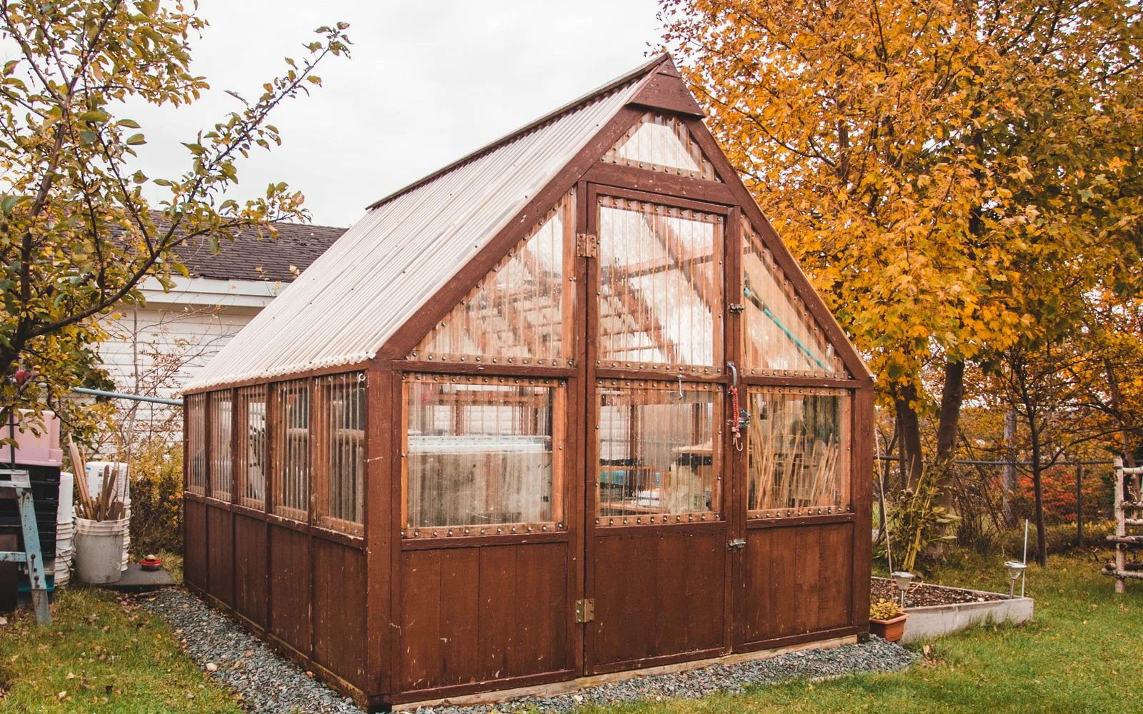 Wooden frame greenhouse with clear panels surrounded by autumn foliage